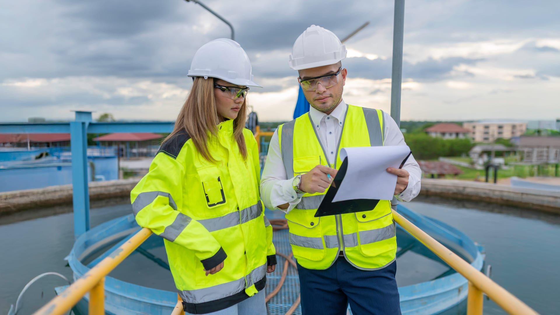 Dos consultores de ingeniería ambiental revisando datos técnicos en una planta de tratamiento de aguas industriales